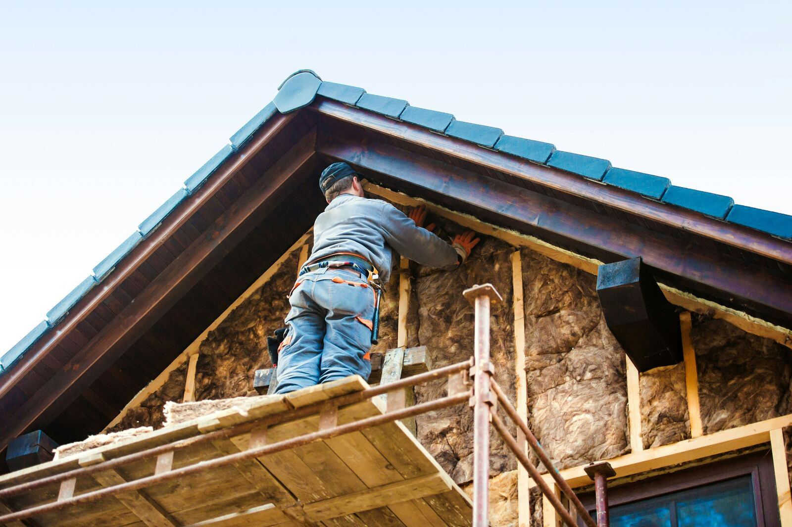 Contractors applying external wall insulation boards to a house facade with scaffolding in place.