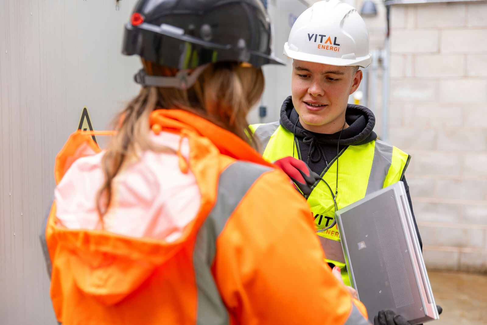 Two site workers in hi-vis collaborating with a laptop on a project handover.
